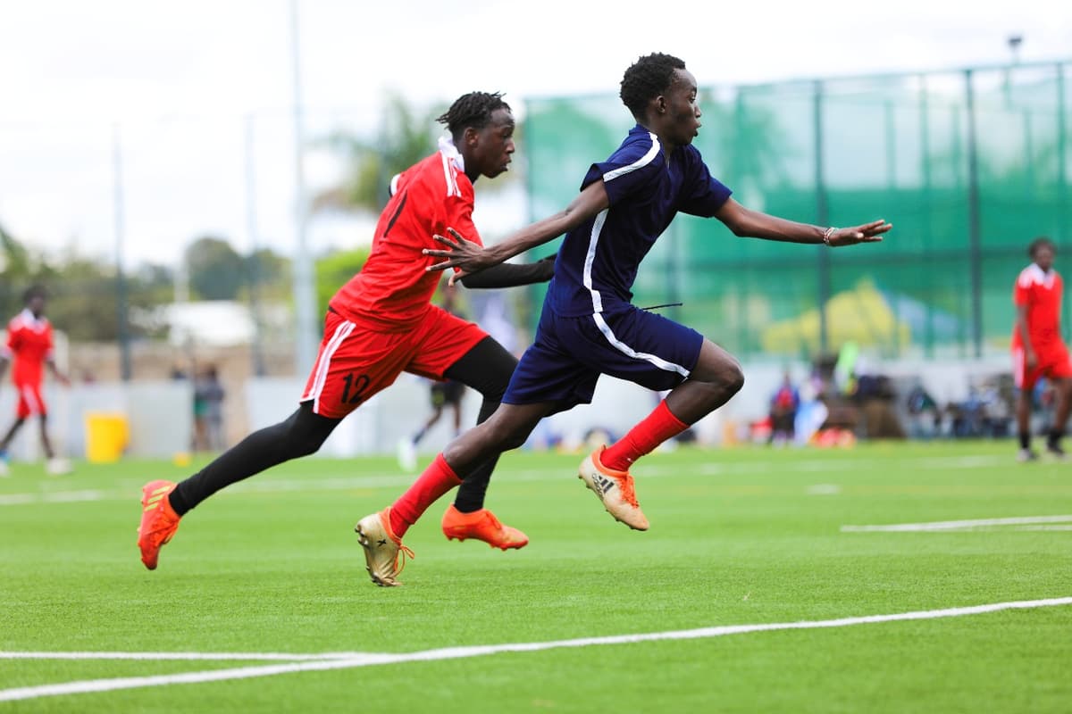 Two young academy players sprinting at full pace during a match, one in red and one in navy