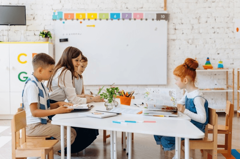 Teacher working alongside young students at a classroom table